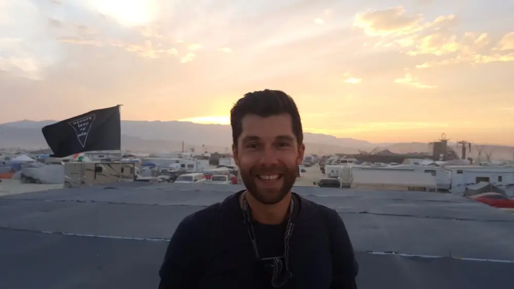 Danny at Burning Man, smiling in front of a golden desert sunset.